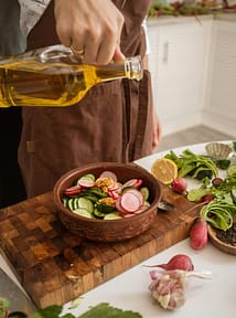 pexels-photo-8978879-8978879 Close-up of fresh salad preparation with olive oil, radishes, cucumber, and greens.